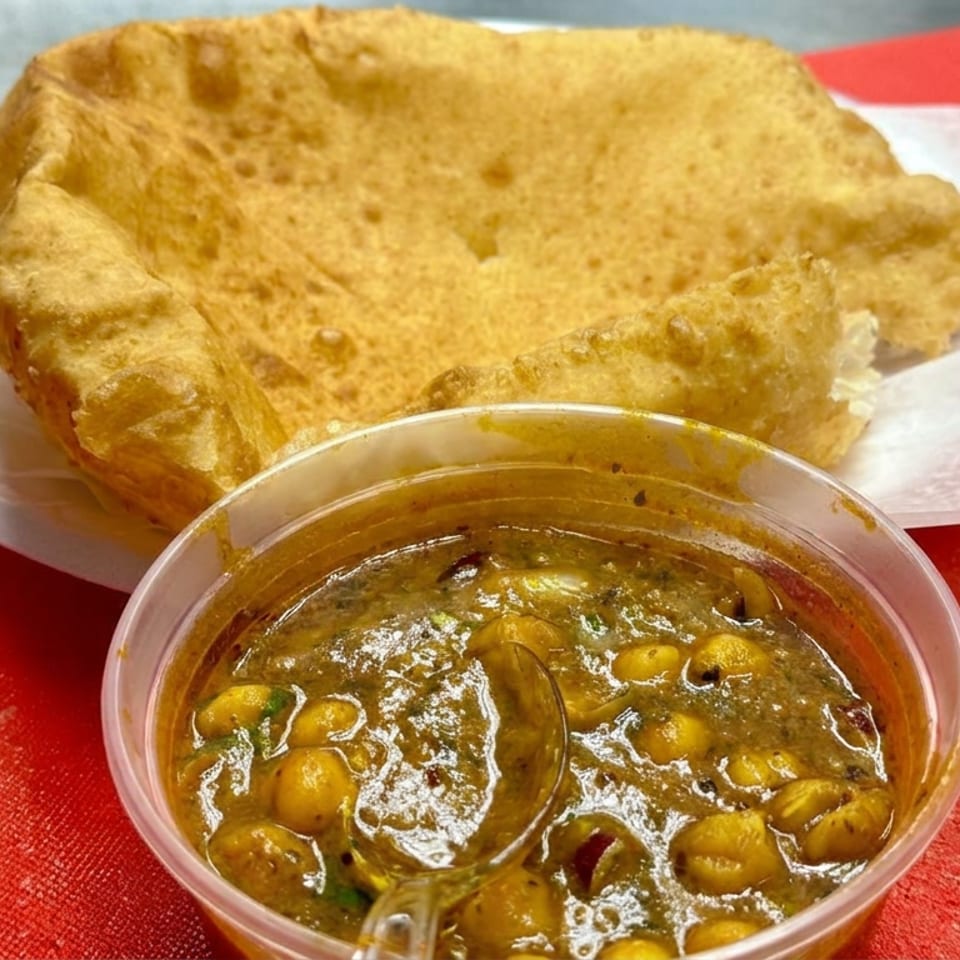 A large golden fried flatbread sits beside a bowl of chickpea curry on a red tablecloth.
